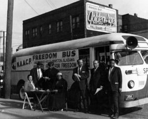 Historic black and white photograph. Group of people sitting and standing by an NAACP freedom bus.